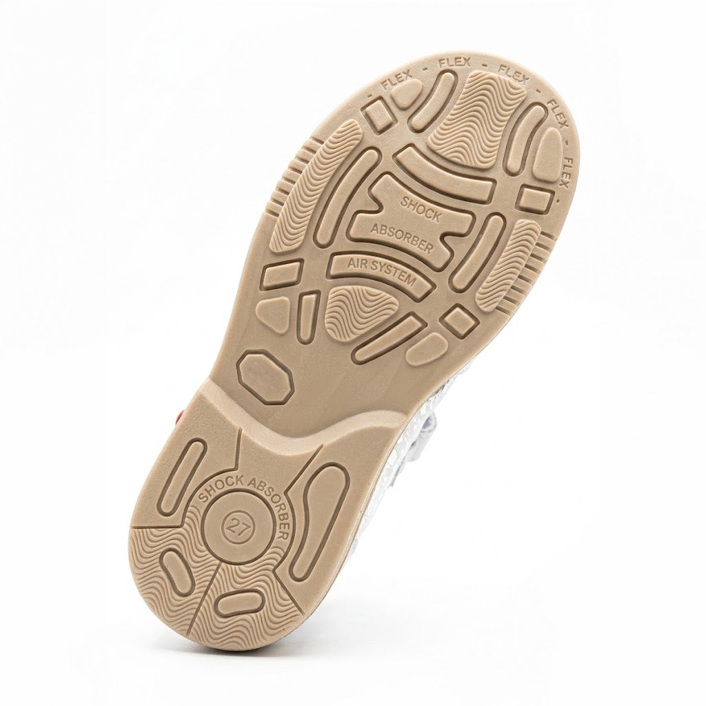 Underneath view of a tan kids shoe sole featuring impact absorption patterns, Air System, and shock absorber tread.