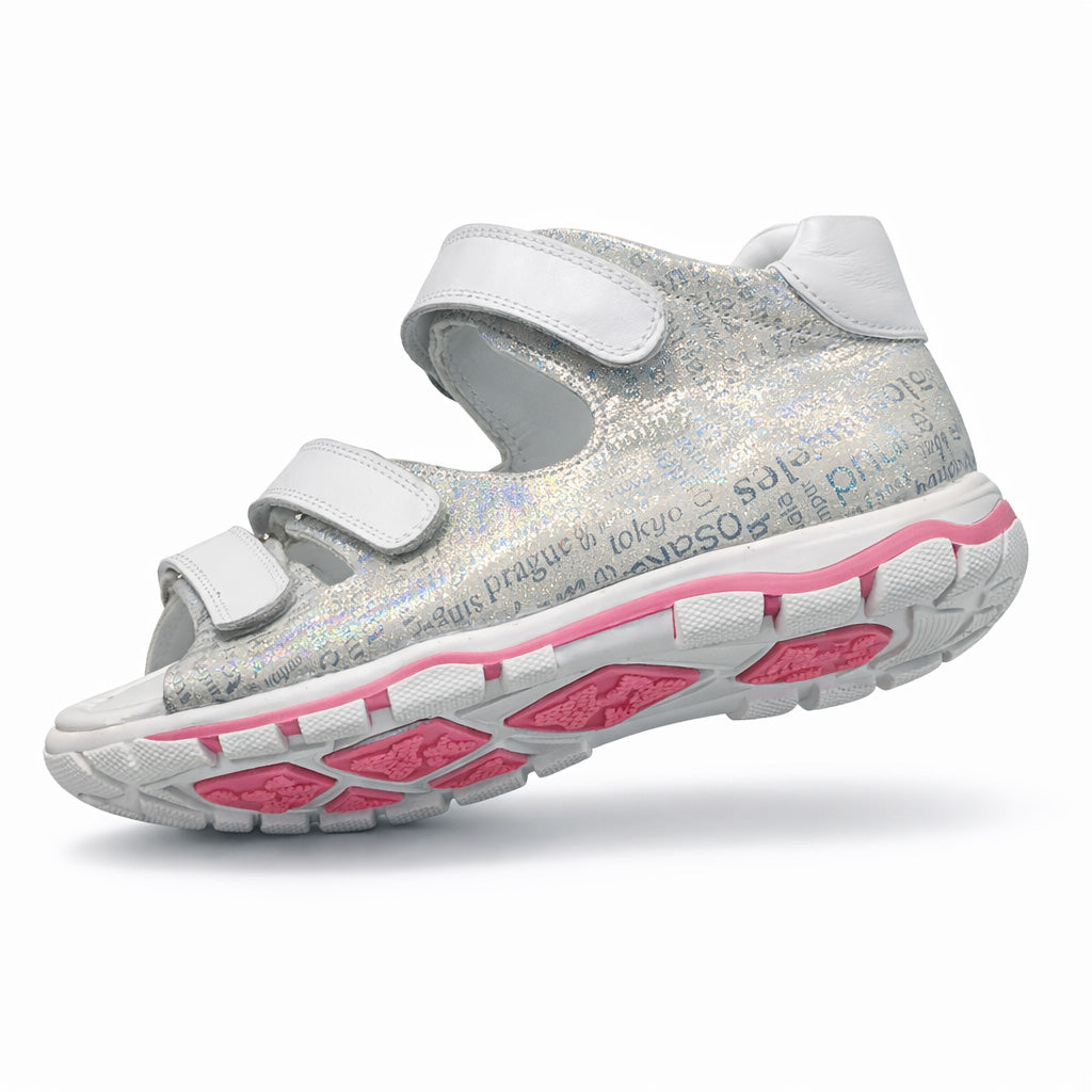 Girls’ orthopedic sandals in silver with white Velcro straps, arch and ankle support, and city-name print by Ortho Shoes.