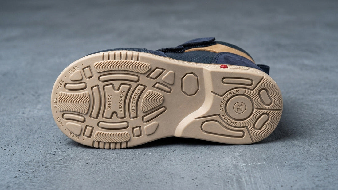 Close-up landscape view of the engineered rubber outsole tread pattern on a children's orthopaedic shoe, showing deep flex channels and a wide, stable base layout.
