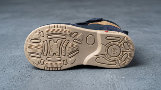 Close-up landscape view of the engineered rubber outsole tread pattern on a children's orthopaedic shoe, showing deep flex channels and a wide, stable base layout.
