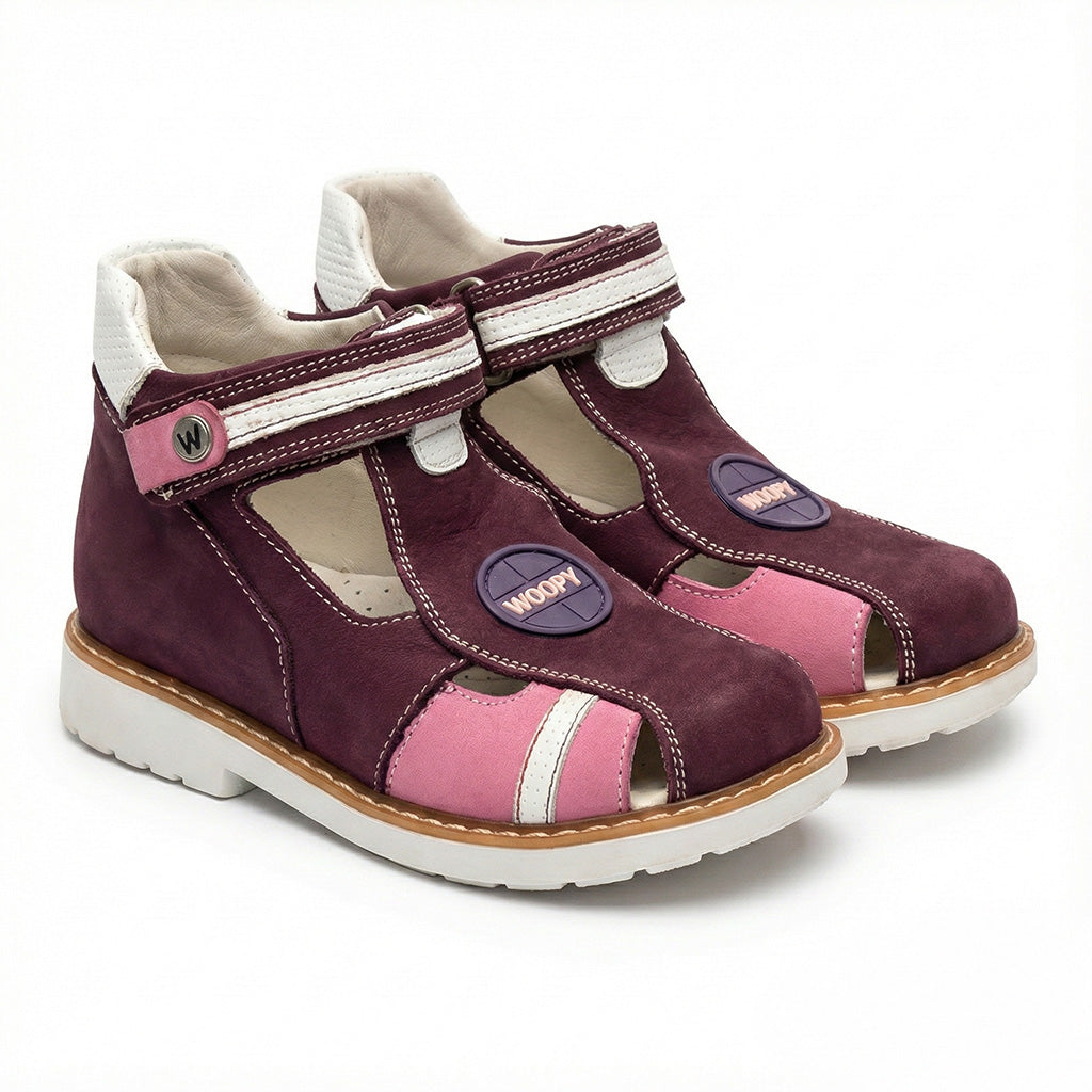 Pair of dark purple children’s orthopedic sandals with pink and white accents, Velcro strap, ‘WOOPY’ branding, arch and ankle support, and Thomas heels.
