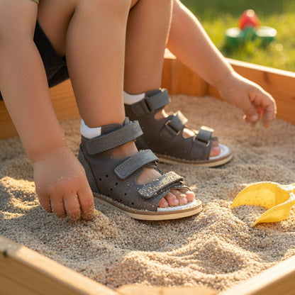 Boy playing in sandbox wearing gray Ortho Shoes kids’ orthopedic sandals with arch and ankle support, Thomas heels and leather lining.