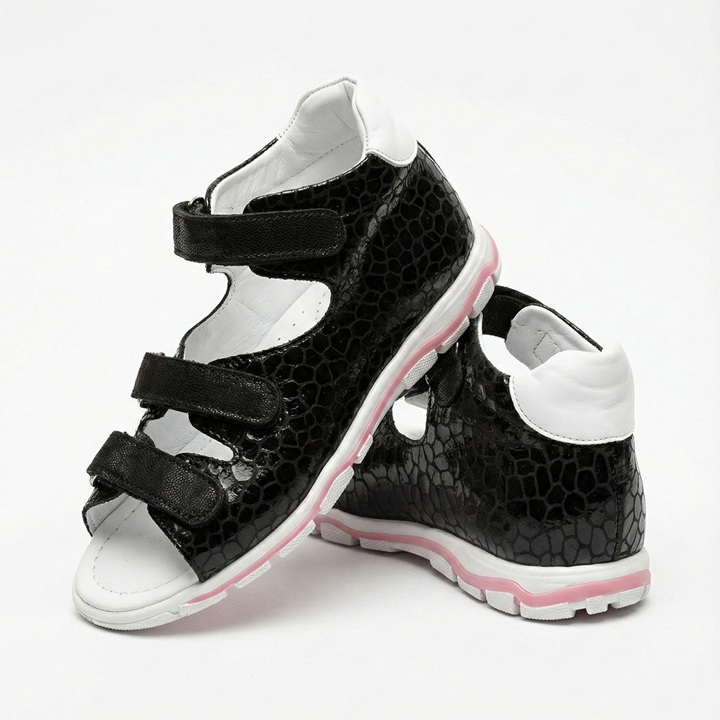 Children’s black orthopedic sandals with reptile-textured finish, white interior, and pink-accented sole.