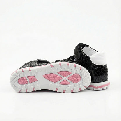 Children’s black orthopedic sandals with reptile-textured finish, white lining, and pink-accented sole.