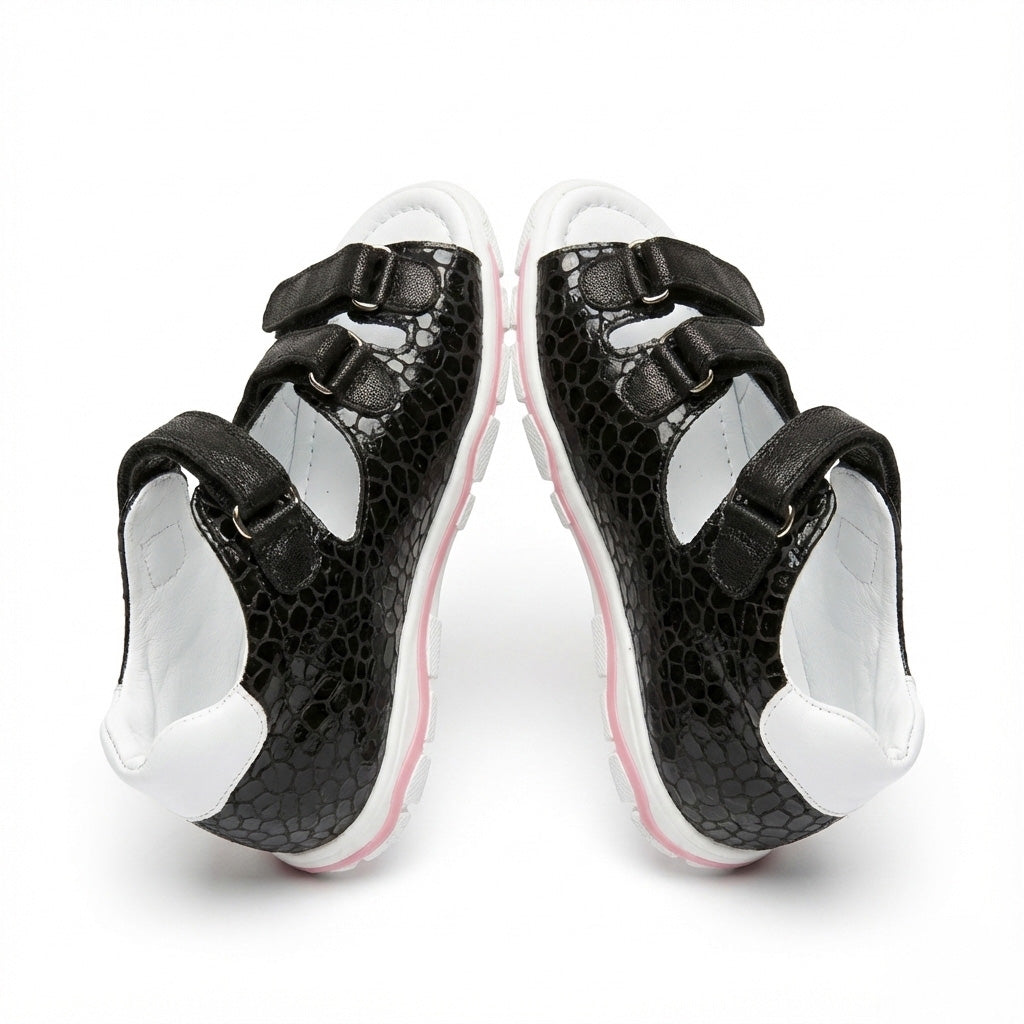 Girls’ orthopedic sandals in black with Velcro closure, arch and ankle support, and pink sole accent.