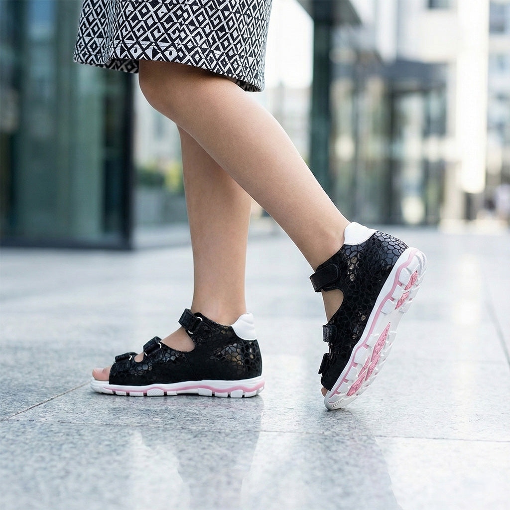 Girl’s orthopedic sandals in black with Velcro straps, pink and white sole and arch support.