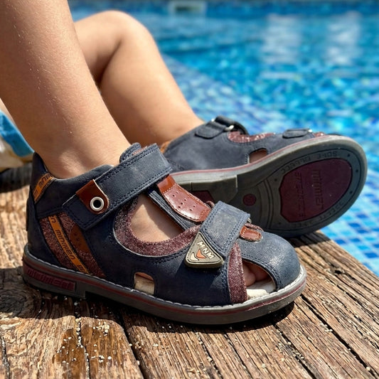 Kids’ navy-brown orthopedic sandals , supportive sole and ankle, and Minimen branding, pictured beside a swimming pool.
