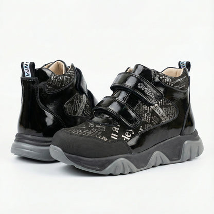 Children’s orthopedic shoes in black with Velcro straps, printed design, arch support, and Thomas heels by Ortho Shoes.