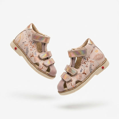 Girls’ orthopedic sandals in pink with Velcro straps, arch and ankle support, Thomas heels and iridescent underwater‑animal print, shown in a retro ice‑cream shop by Ortho Shoes.