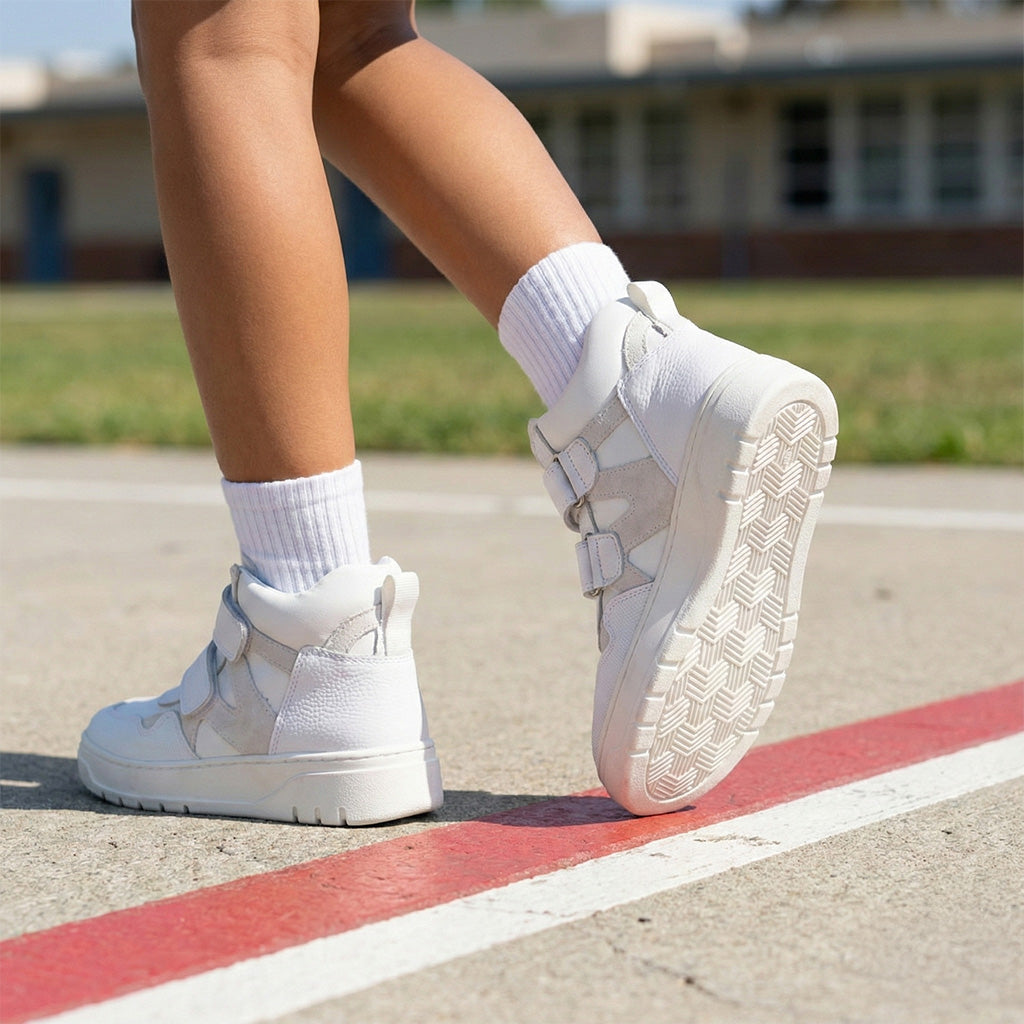 Children’s white orthopedic high-top sneakers with Velcro straps, ankle support, and non-slip sole for school wear by Ortho Shoes.