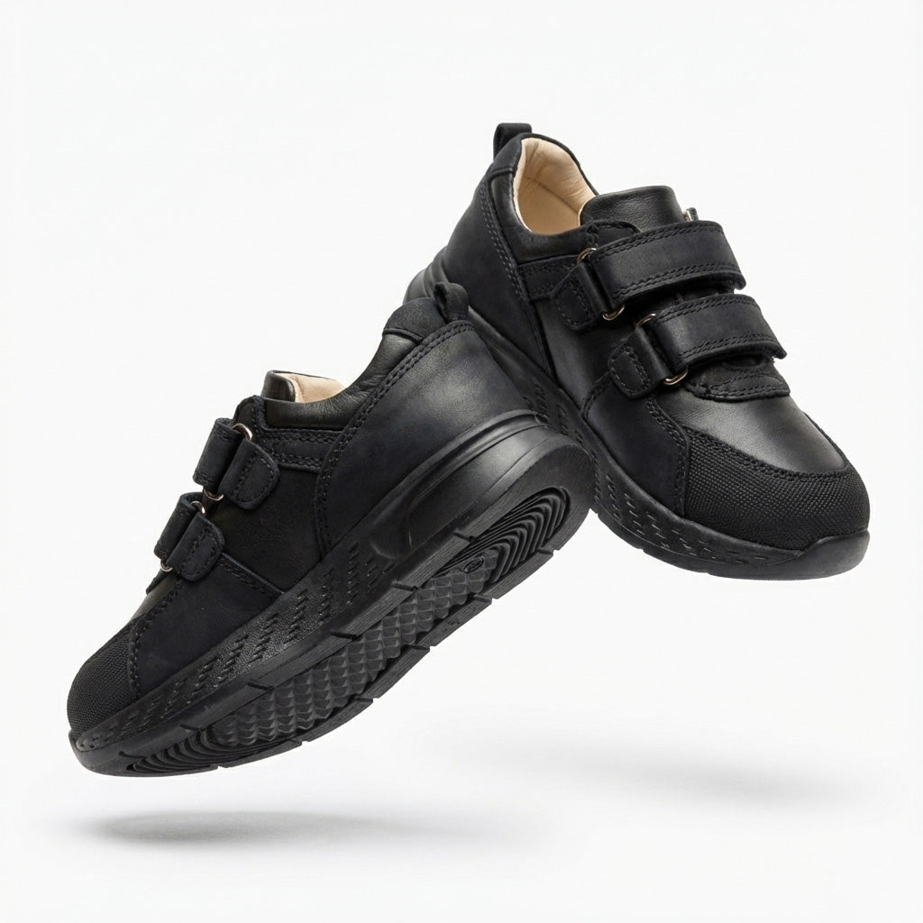 Children’s low-top black school sneakers with Velcro straps, cushioned sole, ankle support and uniform-ready design for indoor wear by Ortho Shoes.