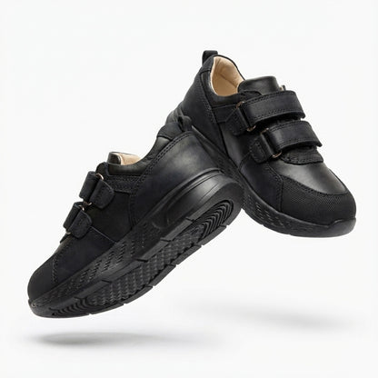 Children’s low-top black school sneakers with Velcro straps, cushioned sole, ankle support and uniform-ready design for indoor wear by Ortho Shoes.