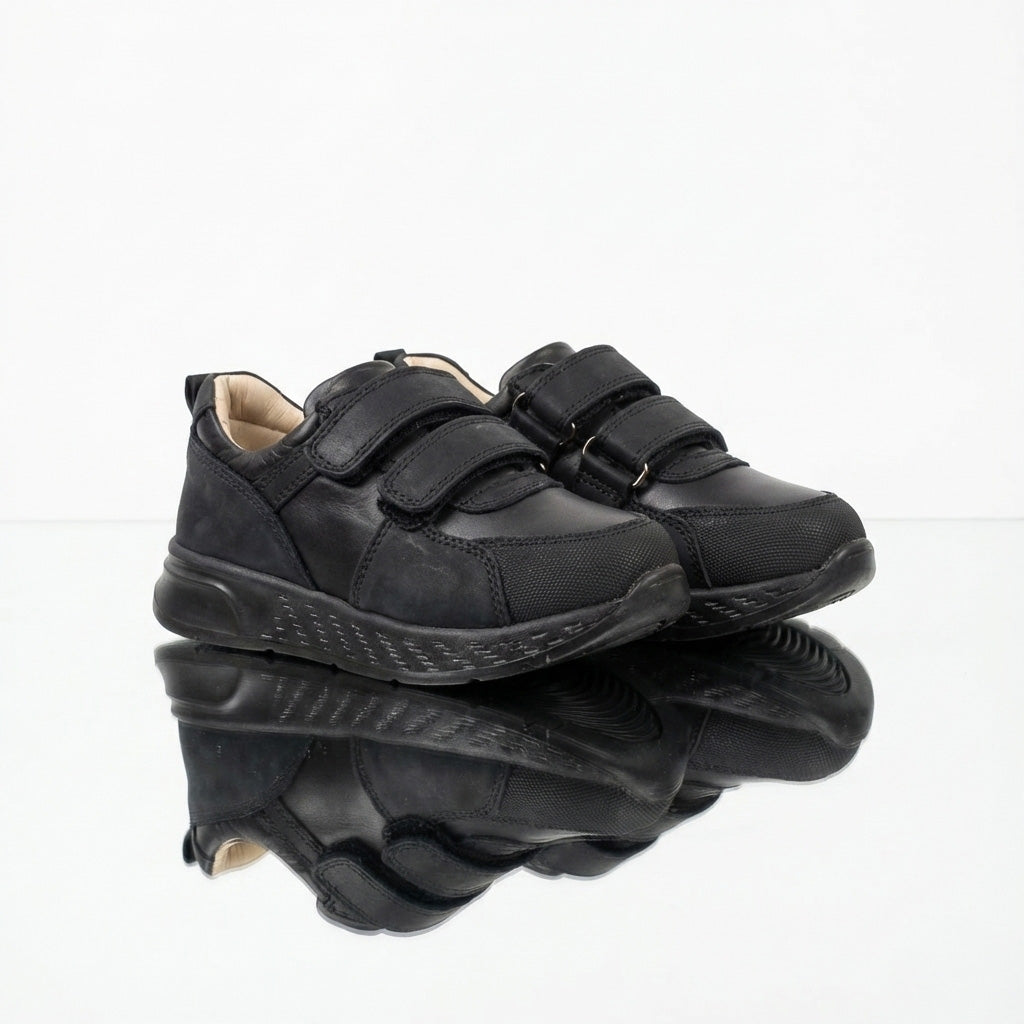 Children’s low-top black school sneakers with Velcro straps, cushioned sole, ankle support and uniform-ready design for indoor wear by Ortho Shoes.