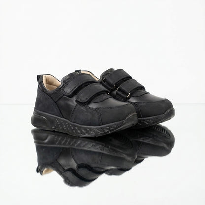 Children’s low-top black school sneakers with Velcro straps, cushioned sole, ankle support and uniform-ready design for indoor wear by Ortho Shoes.