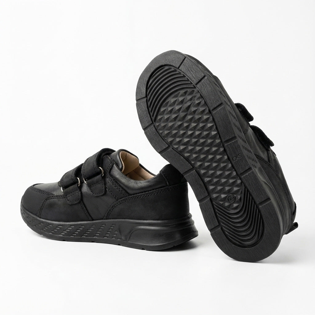 Children’s low-top black school sneakers with Velcro straps, cushioned sole, ankle support and uniform-ready design for indoor wear by Ortho Shoes.