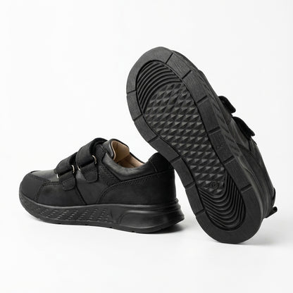Children’s low-top black school sneakers with Velcro straps, cushioned sole, ankle support and uniform-ready design for indoor wear by Ortho Shoes.